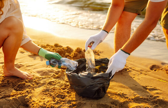 Young friends actively participate in beach cleanup. Cheerful volunteers collect plastic waste and trash along the coastline at sunset. The concept of ecology, ecology and recreation.