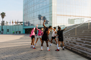 The young athletes exercise outdoors near a modern glass building. They stretch in a circle and wear athletic clothing on a paved urban plaza. © Drobot Dean
