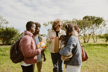A multinational group of young people standing together on a grassy field during a sunny day,...