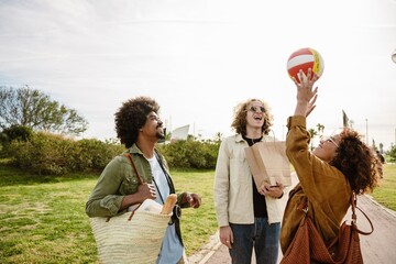 Three friends enjoy a sunny day in the park, laughing together as one of them reaches up to catch a...