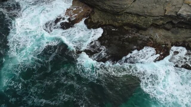 Stunning aerial views of frothy white ocean waves colliding with dark rocks along the rugged coastline of Cape Zemlyanov in the Barents Sea.