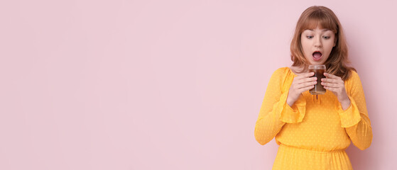 Surprised young woman with glass of tasty iced latte on pink background