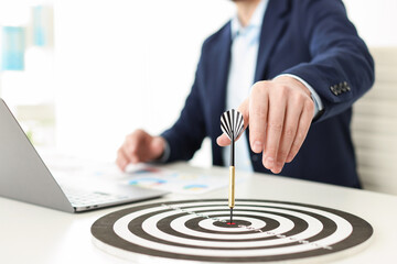 Man working on laptop at table, focus on dartboard with arrow indoors