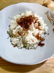 White rice with fried onions on top on a white plate with floral motifs on a wooden table. rice as food