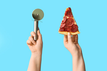 Female hands holding tasty pizza slice and pizza cutter on blue background
