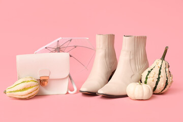 Stylish boots with white bag, umbrella and pumpkins on pink background