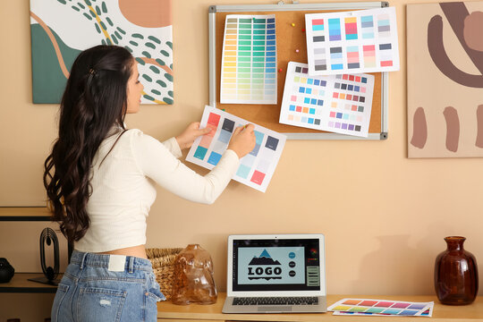 Young female graphic designer pinning color palette on cork board in office