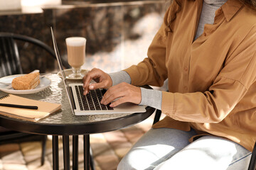 Female author using laptop at table in street cafe, closeup