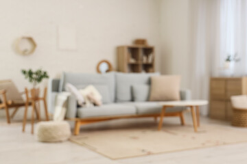 Blurred view of living room with grey sofa, table and shelf unit