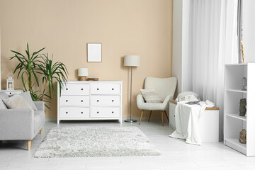 Interior of light living room with chest of drawers, sofa and armchair near beige wall