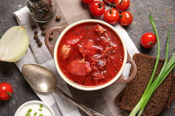 Bowl of tasty Ukrainian borscht with bread slices and ingredients on dark background