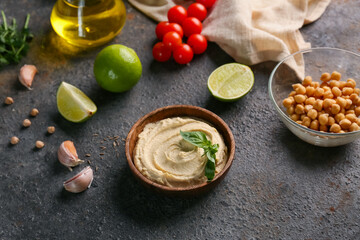 Bowl of tasty hummus with ingredients and napkin on black grunge background, closeup