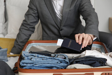 Young businessman packing passport into suitcase for trip in bedroom, closeup