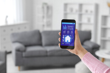 Female hand holding mobile phone with smart home security system control panel in room