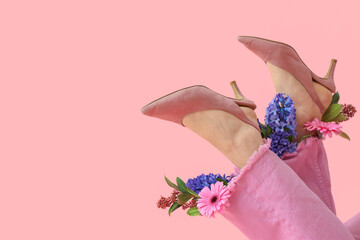 Legs of young woman in stylish high heels with beautiful flowers on pink background