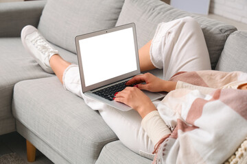 Young woman with cozy blanket and laptop lying on sofa at home