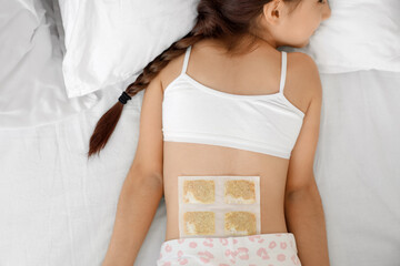 Ill girl with mustard plaster on her back lying in bedroom, top view