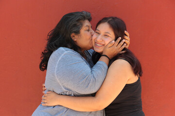 A 50-year-old Latina mother and her 18-year-old daughter hug and kiss each other to show their love and celebrate Mother's Day