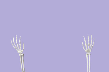 Raised hands of human skeleton on lilac background
