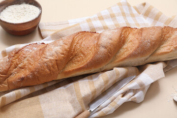 Fresh baguette and wooden bowl of flour on beige background, closeup