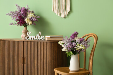 Interior of living room with chair, commode and lilac flowers in vases