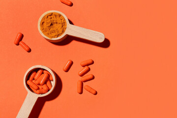 Scoops with turmeric powder and pills on orange background, top view