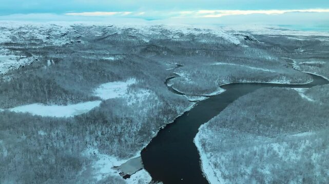 Frozen Titovka River stretches through vast white wilderness in Arctic Russia as drone reveals snow-coated tundra and icy river path.