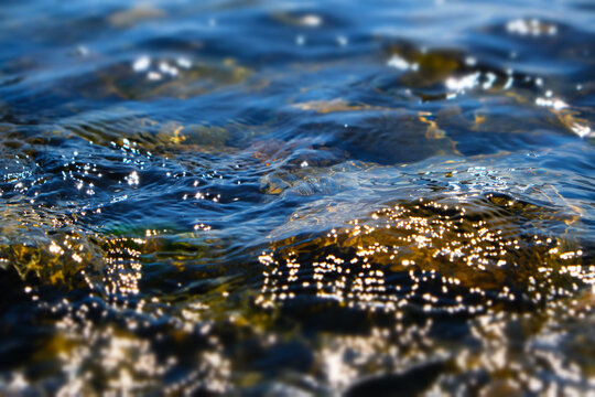 Cristal river, waterfall glowing water background, stones, rapids and boulders. Texture clear cold sea water with reflection sunlight. Falling and flowing water. Scenery lake. Shallow DOF