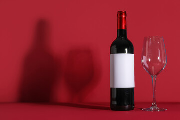 Bottle of wine with blank label and empty glass on red background