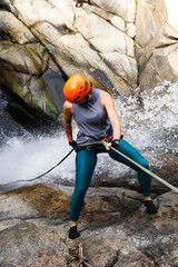 Adventurous woman rappelling down a stunning waterfall, embracing the thrill of extreme sports in a...