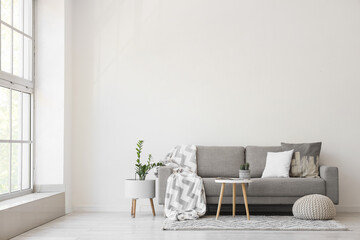 Interior of light living room with grey sofa, table and pouf