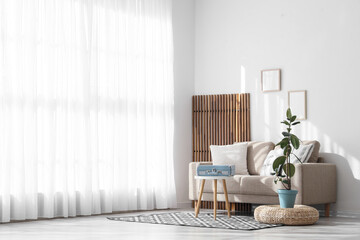 Interior of light living room with grey sofa, table and folding screen