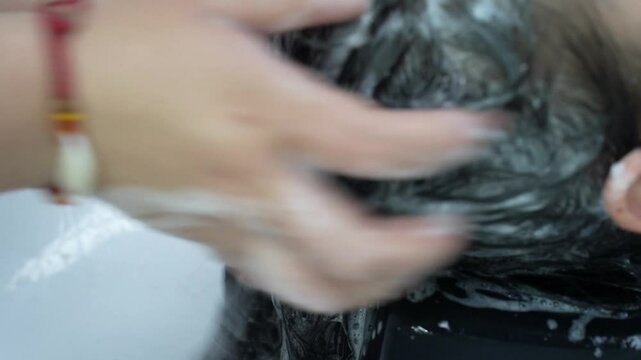 Asian young woman lying down on salon washing bed getting hair washed in hair salon by stylist.