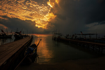 Fototapeta premium Background of golden sunlight in the morning by the sea, with fishing boats moored at the pier, waiting for the time to go out to fish again.