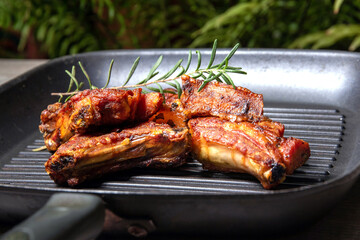 Grilled Pork Ribs on a Cast Iron Grill with Rosemary – Juicy BBQ Meat on a Rustic Outdoor...