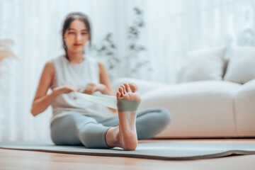 Young Asian woman doing pilates workout using elastic strap pulling with arms for shoulder training on yoga mat indoors. Resistance band exercise at home