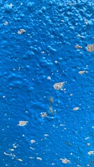 The background of the wall features a blend of blue and white tones, with uneven patches and subtle traces of paint that give it a weathered, textured appearance. The overlapping colors and visible br