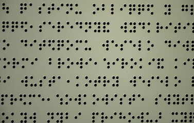 Embossed braille text on beige surface. Tactile writing system for visually impaired and blind people. Accessibility and communication concept.