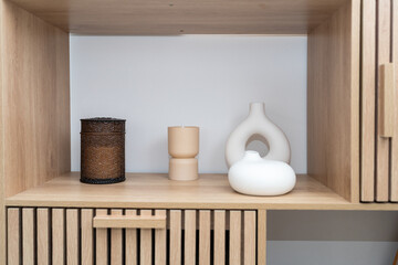 A wooden shelf holds an assortment of decorative items including a textured container, a candle holder, and a smooth ceramic piece. The arrangement is visually appealing and minimalist.
