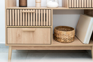 A stylish wooden shelf features decorative pieces, a woven basket, and an open storage space. Natural light highlights the minimalist design and warm tones of the wood.