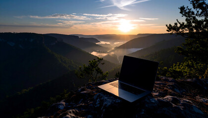 Laptop on a rocky cliff overlooking a foggy valley at sunset.