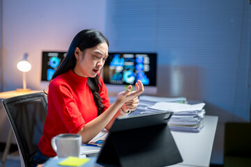 A woman in a red shirt is sitting at a desk with a laptop and a cup of coffee