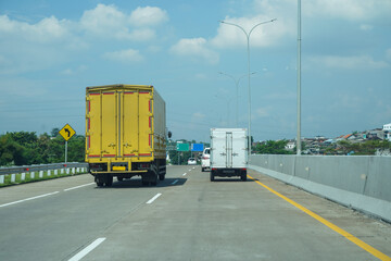 Trucks Driving on Highway Under Blue Sky with Urban Background and Traffic Sign