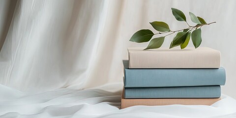 Stacked books with greenery on a draped background.