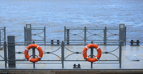 Red lifebuoys hang on the fence of the river pier