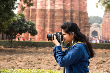 Young woman photographer with DSLR camera at Qutub Minar , Delhi, India.