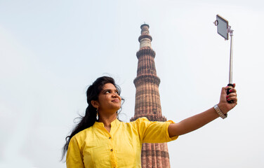 Tourist woman taking selfie in front of Qutub Minar, Delhi, India.