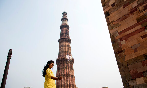 Tourist woman taking selfie in front of Qutub Minar, Delhi, India.