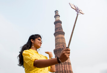 Tourist woman taking selfie in front of Qutub Minar, Delhi, India.