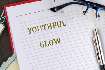 A notebook lies open on a desk, featuring the phrase youthful glow in bold lettering. Nearby,...